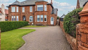 A brick house with a paved driveway, a well-maintained lawn, and a hedge. - The Bay Suite - Donnini Apartments (Troon)