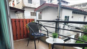 Un balcón con una silla de mimbre, una mesita con una planta en maceta y vistas a edificios.