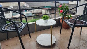 Un balcón con dos sillas de mimbre, una mesa redonda pequeña y plantas en macetas.