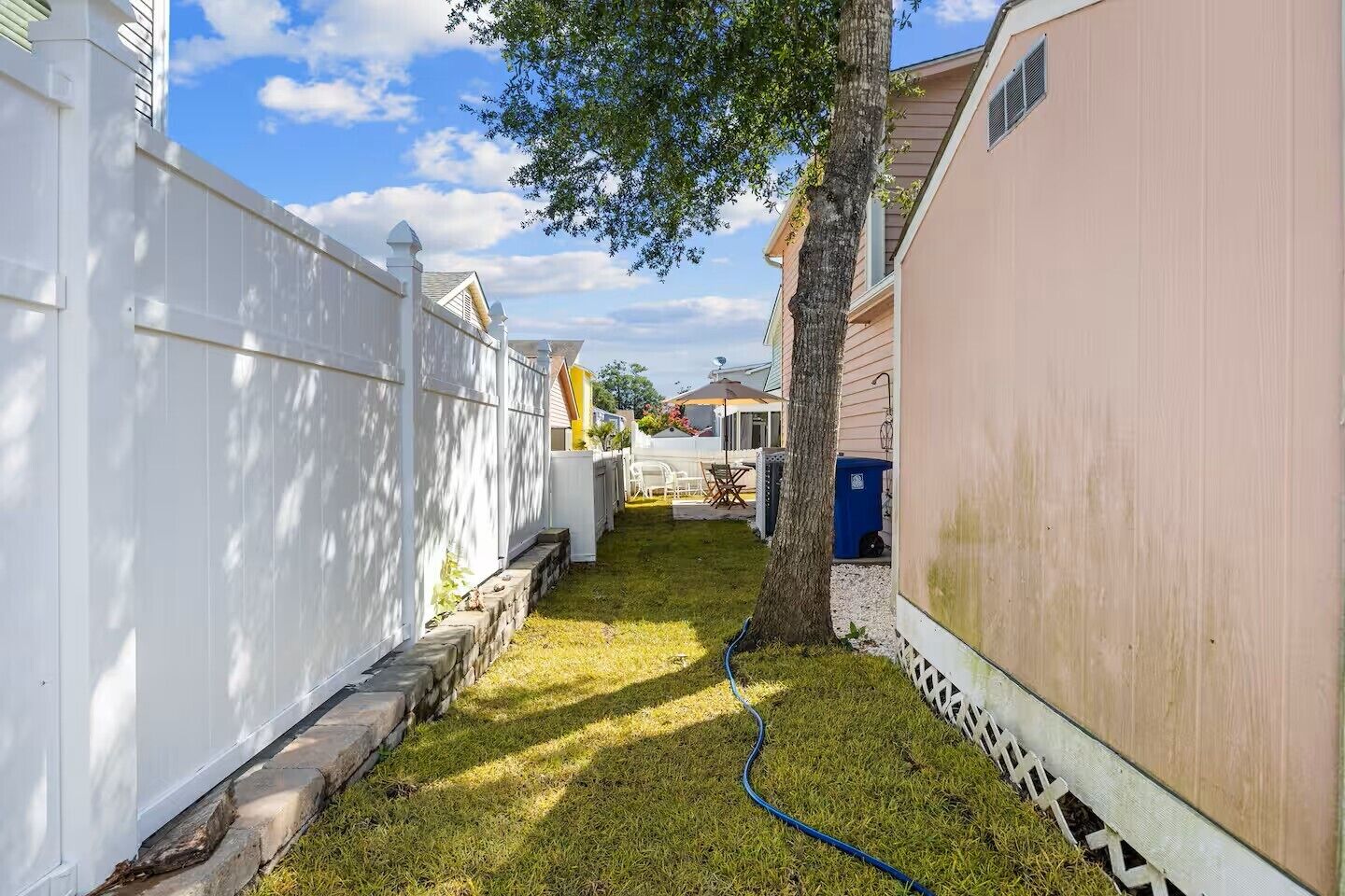 Un petit jardin à l’arrière de la maison, avec une clôture blanche, un arbre et un tuyau d’arrosage.