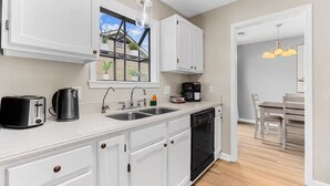 Una cocina moderna con armarios blancos, lavavajillas integrado, cafetera y ventana con vista a un balcón.