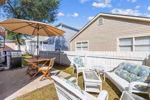 A backyard with a grill, outdoor furniture, and a white fence.