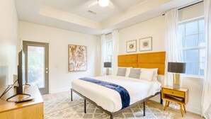A bedroom with a bed, a desk, a TV, and a window with curtains.