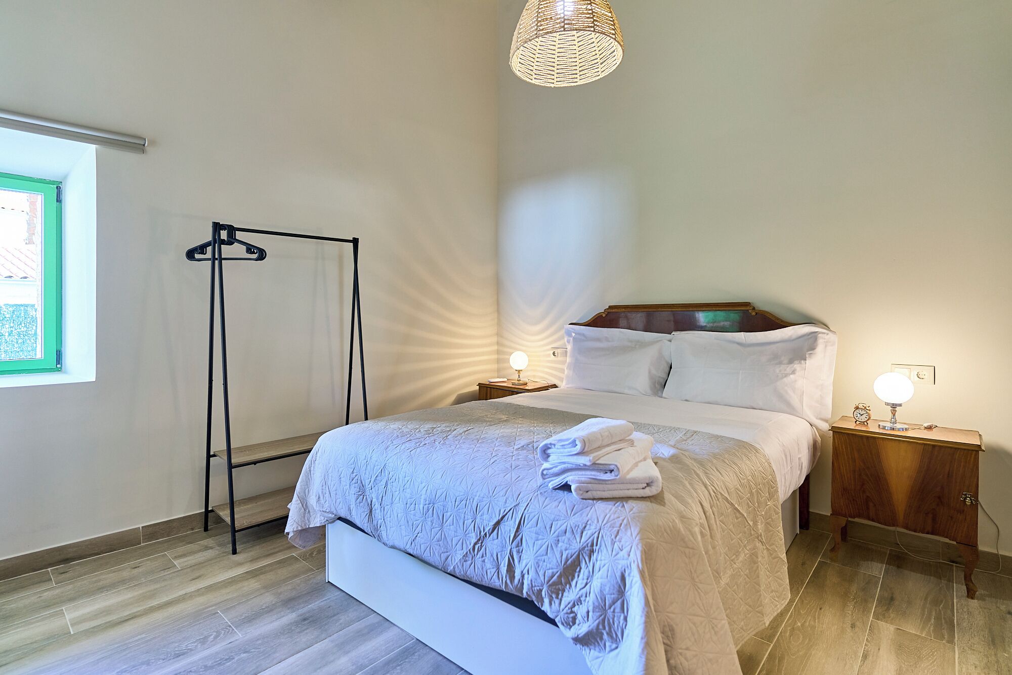 A neatly made bed with a folded towel, a bedside table with a lamp, and a hanging light fixture.