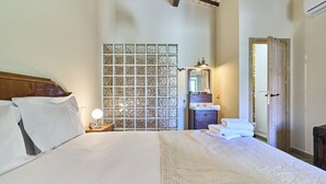 Ein Schlafzimmer mit einem großen Bett, einem Nachttisch mit Lampe, einer Kommode, einem Spiegel und einer Tür.
