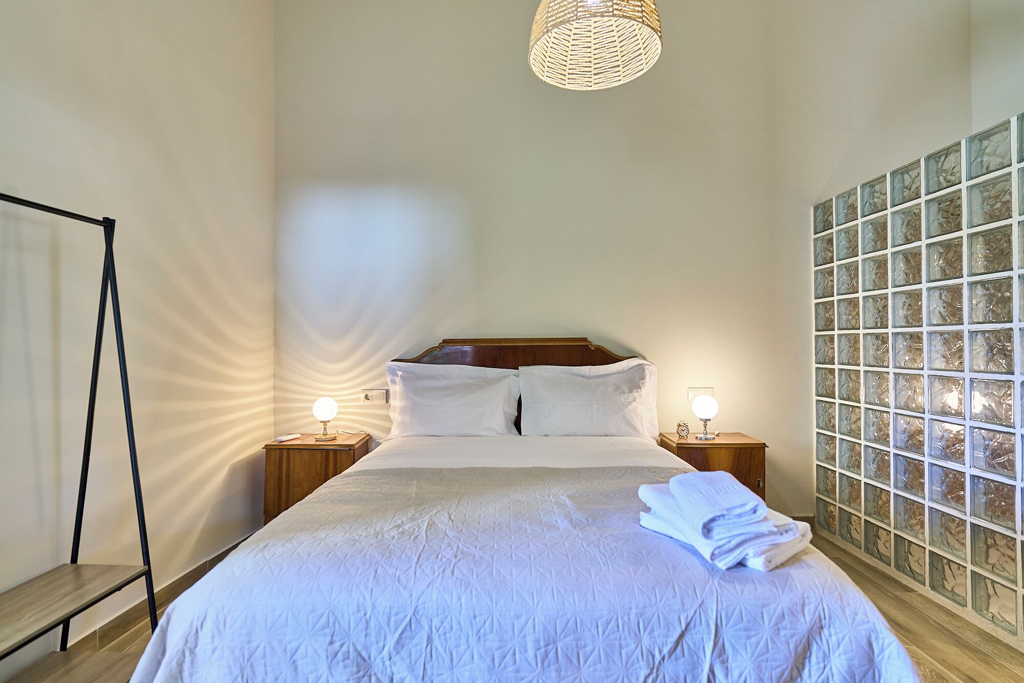 A neatly made bed with white bedding, two bedside lamps, a wooden headboard, and a wall with a patterned window.
