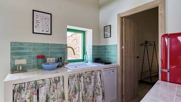 A kitchen with a sink, a dish rack, a red refrigerator, and a window with a green frame.