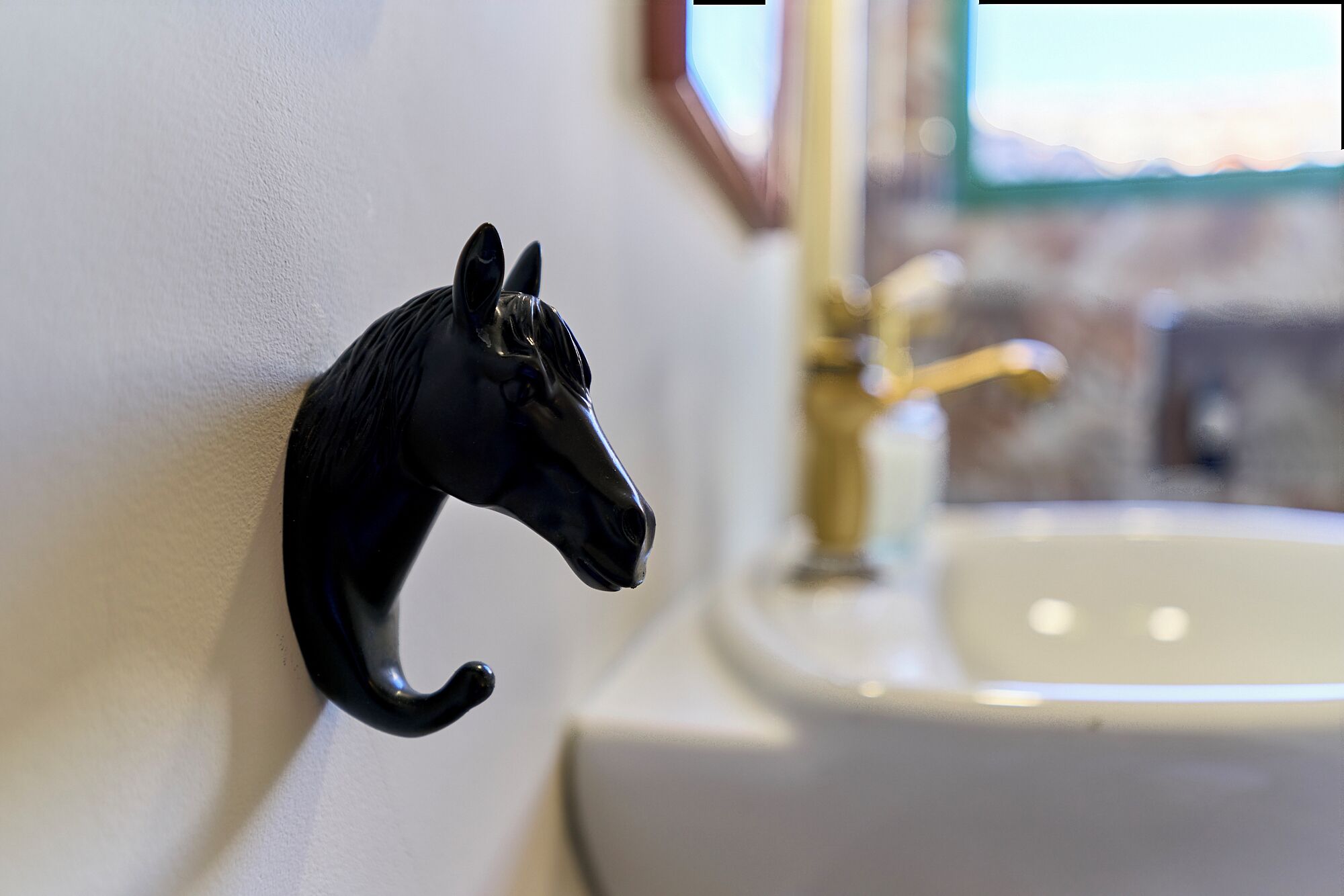 A black horse-shaped hook on a white wall near a bathroom sink.