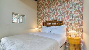 Un dormitori amb un llit, dues làmpades de nit, una finestra i una paret amb un dibuix floral.