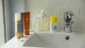 A bathroom sink with toiletries including a bottle of shampoo, a bottle of liquid soap, and a tube of cream.