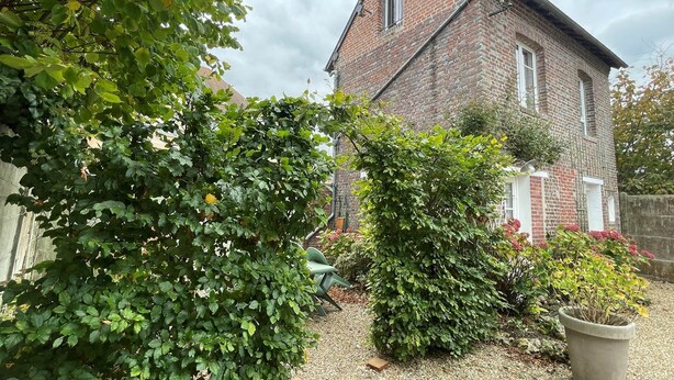 A brick house with a garden, a gravel driveway, and a green bush in the foreground.