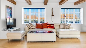 A spacious living room with a white sofa set, a coffee table, and a TV on a stand. There are large windows with a view of buildings outside. - "Albine" - 150m from the sea by Interhome (Skagen)