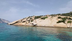 Eine Küstenlandschaft mit klarem türkisblauem Wasser, einem felsigen Landvorsprung mit vereinzelter Vegetation und einem entfernten Berg.