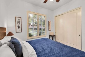 A bedroom with a bed, a window with blinds, a door, and framed artwork on the walls.
