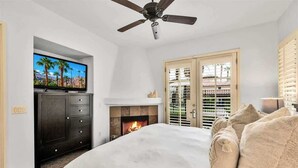 Une chambre à coucher comprenant un lit, une télévision, une cheminée et un ventilateur de plafond.