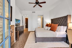 A bedroom with a large bed, a ceiling fan, a television, and a dresser.