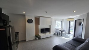 Un salon moderne doté d’un téléviseur à écran plat, d’un coin repas avec une petite table et des chaises, d’un canapé et d’une horloge murale.
