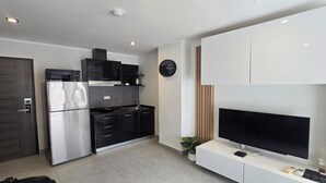 Une cuisine moderne équipée d’un réfrigérateur, d’un four à micro-ondes, d’une cuisinière et de placards. Il y a une horloge au mur et un téléviseur posé sur un meuble.