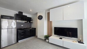 Une cuisine moderne avec des appareils en acier inoxydable, un téléviseur à écran plat posé sur un meuble blanc et une horloge au mur.