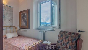 A bedroom with a bed, a chair, a window with a view, a radiator, and a framed picture on the wall. - Varenna Wonders  (Varenna)