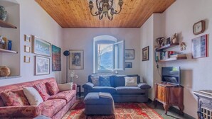 A cozy living room with a wooden ceiling, a large window, a fireplace, and a television. - Varenna Wonders  (Varenna)