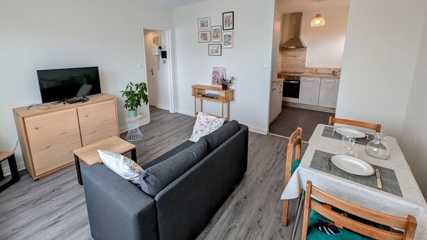 Una sala moderna con sofá, televisor y comedor con sillas y una mesa.