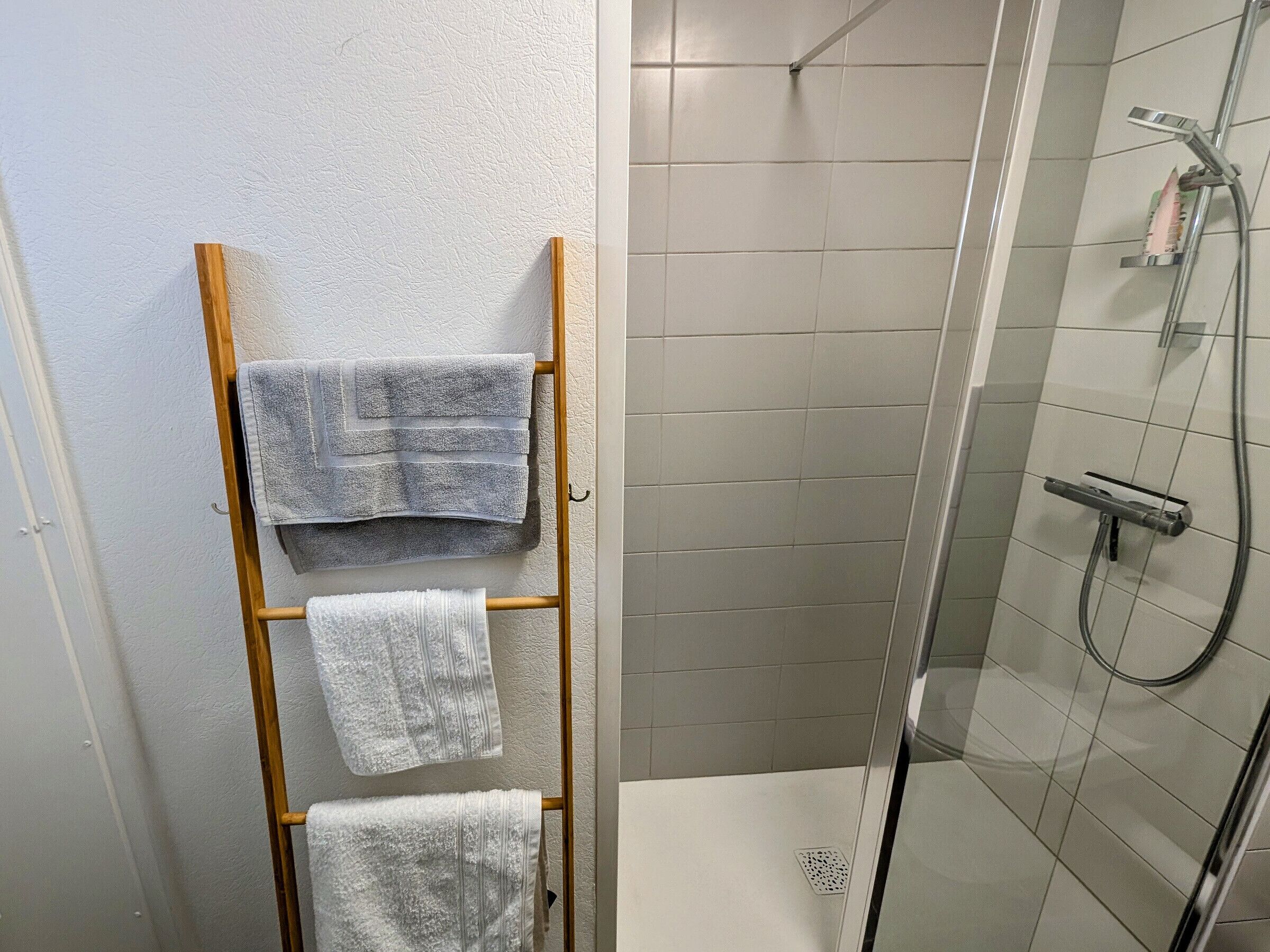 Un espace douche doté d’une porte en verre, d’un porte-serviettes avec deux serviettes et d’un pommeau de douche.
