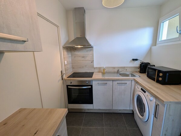 A compact kitchen with a built-in oven, microwave, sink, and washing machine. - Cozy apartment in the heart of Luxeuil-les-Bains near spas (Luxeuil-les-Bains)