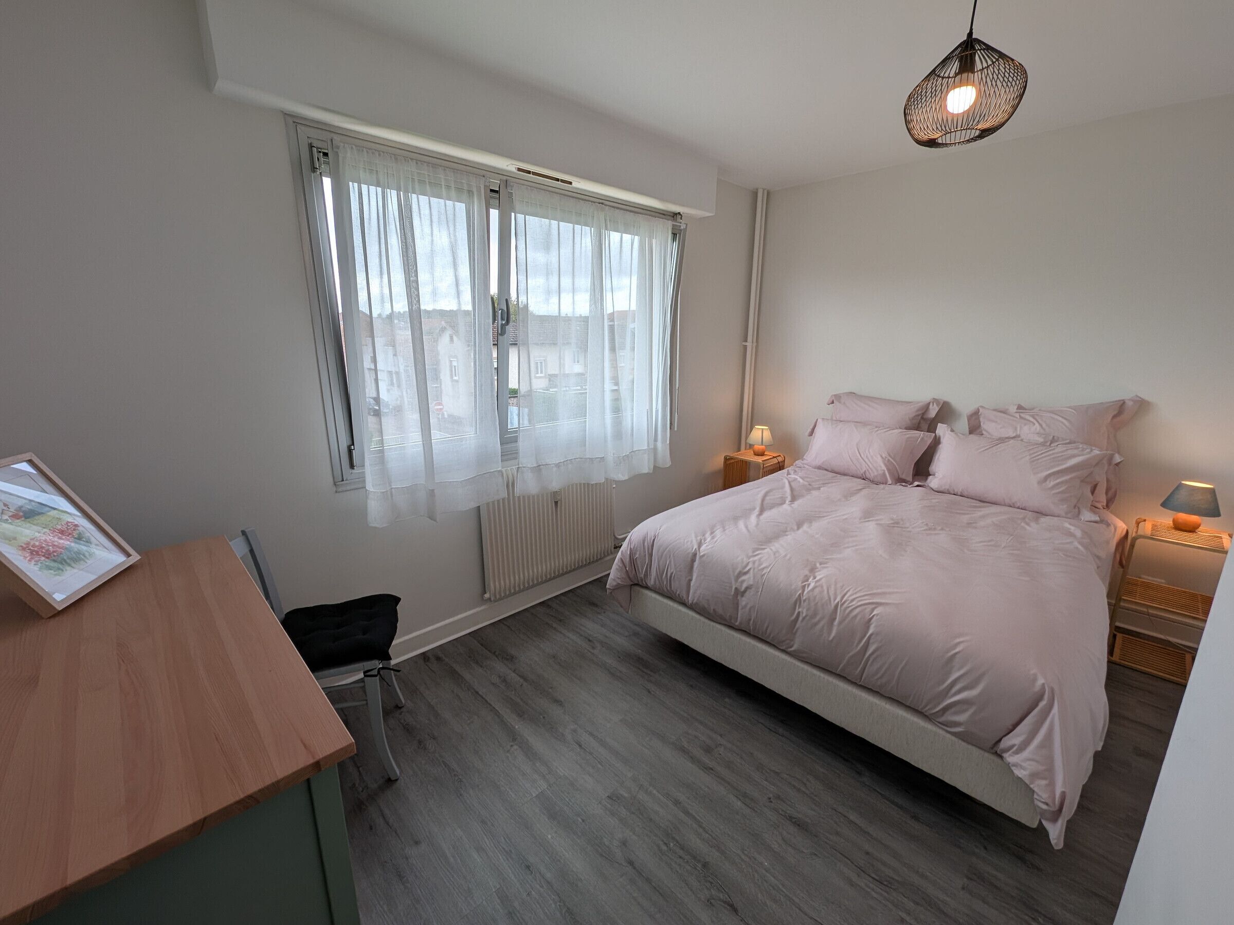 Een slaapkamer met een bed, nachtkastjes, een bureau en een raam met gordijnen.