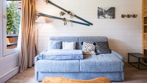 A room with a wooden ceiling, a sofa with cushions, a lamp, a picture on the wall, and a window with curtains.