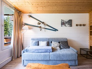 Una habitación con techo de madera, un sofá con cojines, una lámpara, un cuadro en la pared y una ventana con cortinas.