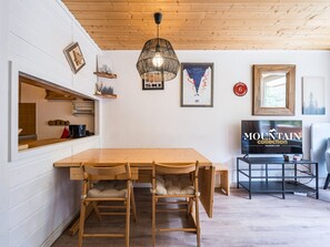 A wooden dining table with chairs, a TV, and framed pictures on the wall. - Central studio 3-4 ppl, near slopes, balcony (Val-d'Isère)
