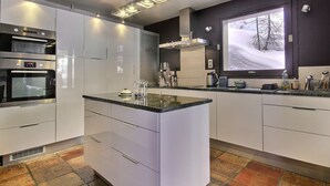 A modern kitchen with white cabinetry, a central island, built-in ovens, and a large window with a snowy view. - Spacious chalet with terrace and jacuzzi, near slopes for 14 people (La Plagne 1800)