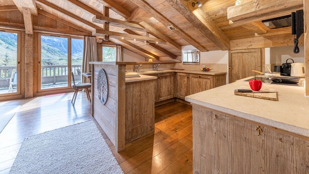 Une cuisine spacieuse avec des poutres en bois, un grand îlot central et une vue sur les montagnes par les fenêtres.