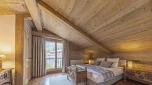 Une chambre confortable située sous les combles, avec un plafond en bois, un grand lit, une table de chevet et une vue sur l’extérieur grâce à une porte coulissante.