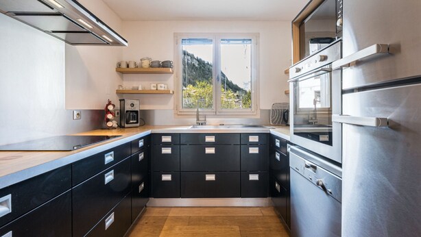 Eine moderne Küche mit schwarzen Schränken, Edelstahlgeräten und einem Fenster mit Blick auf die Berge.