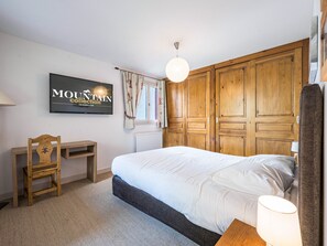 Une chambre à coucher comprenant un lit, un bureau, une chaise, un téléviseur fixé au mur et des armoires en bois.