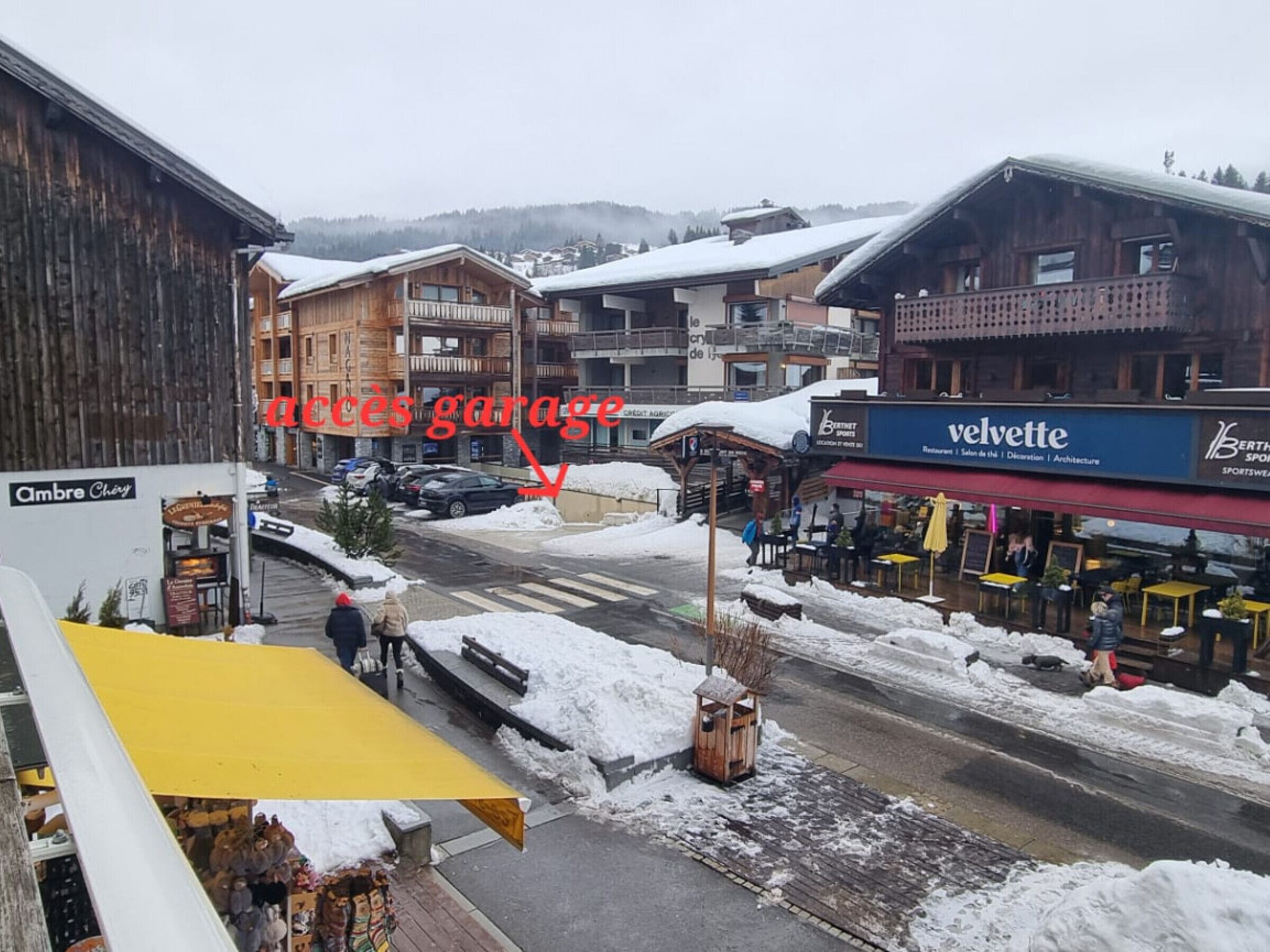 A snowy street with buildings, a yellow awning, and a sign for 'Accès Garage'.