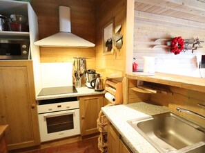 Una cocina compacta con armarios de madera, horno integrado, microondas y pileta de acero inoxidable.