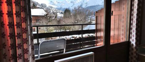 Ein Zimmer mit Blick auf schneebedeckte Berge, einem Holzbalkon und einer Heizung.