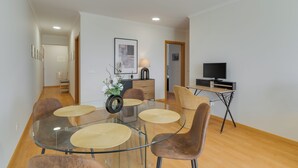 A modern living room with a glass dining table, comfortable seating, a television, and a small kitchen area. - Sun Flower with Oceanview (Caniço)