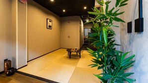 Una habitación japonesa tradicional con suelo de tatami, una mesita con un juego de té, una planta de bambú y un reloj en la pared.