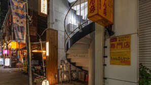 Vista nocturna de una calle con un edificio que tiene un letrero con texto japonés, una escalera y una pequeña tienda con letrero.