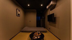 Un estrecho pasillo con suelo de tatami, una mesa baja con una bandeja, un cojín y un televisor montado en la pared.