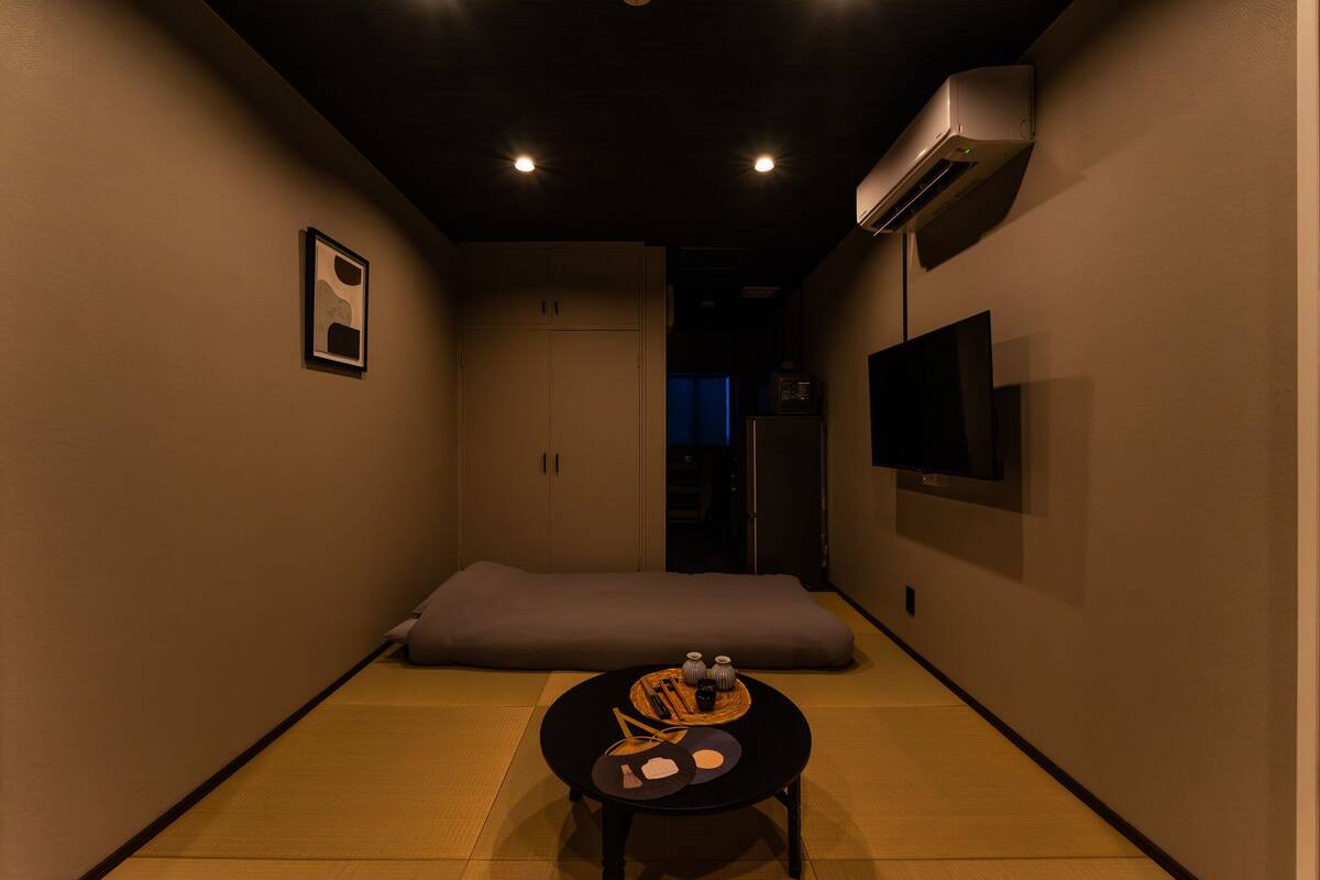 A narrow hallway with a tatami mat floor, a low table with a tray, a pillow, and a wall-mounted TV.