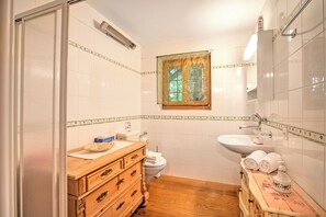 A bathroom with a wooden vanity, a white sink, a toilet, and a window with a decorative frame. - Honeymoon Love Retreat 2 (Minusio)