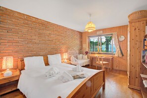 A hotel room with a brick wall, wooden furniture, a bed with white linens, a desk, and a window with a view of greenery. - Honeymoon Love Retreat 2 (Minusio)