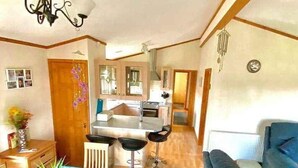 A cozy, well-lit living room with a sofa and a dining area with a table and chairs. - Lodge - Sleeps up to 6, pet Friendly & bbq Allowed (Pwllheli)