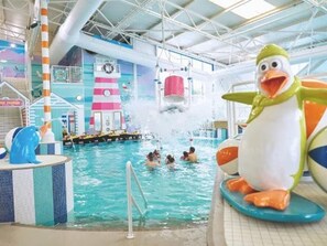 Un parque acuático interior con un gran pingüino inflable, una piscina y diversas estructuras de juegos de agua.