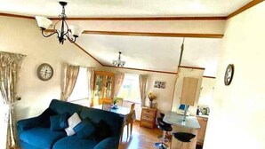 A living room with a blue sofa, a dining table, and a kitchen area with a sink and cabinets. - Lodge - Sleeps up to 6, pet Friendly & bbq Allowed (Pwllheli)